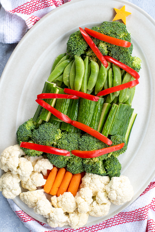 Angled view of a platter with veggies shaped into a Christmas tree complete with red vegetables are decorations and a slice of cheese shaped like a star on top.