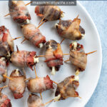 Pinterest Pin with text overlay 'Bacon Wrapped Dates with Goat Cheese'. Image of bacon wrapped dates placed on a white plate.