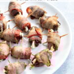 Pinterest Pin with text overlay 'Bacon Wrapped Dates Stuffed with Goat Cheese'. Image of bacon wrapped dates placed on a white plate.