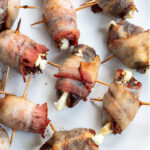 Pinterest Pin with text overlay 'Bacon Wrapped Dates with Goat Cheese'. Image of bacon wrapped dates placed on a white plate.