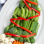 Pinterest Pin with text overlay How to Make A Christmas Tree Veggie Tray. Image of a platter with vegetables shaped into a Christmas tree with decorations.