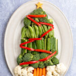 Pinterest Pin with text overlay Christmas Tree Veggie Tray. Image of a platter with vegetables shaped into a Christmas tree with decorations.