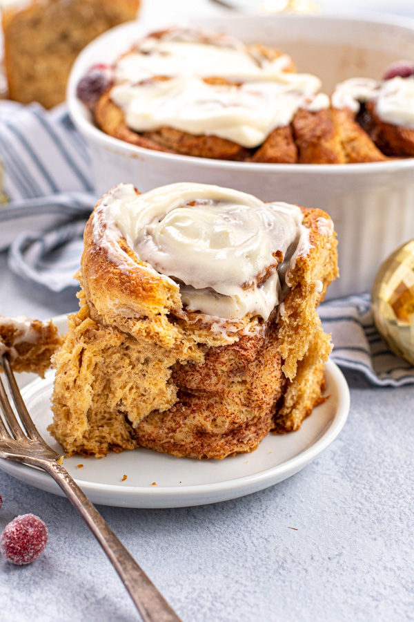 A gingerbread cinnamon roll on a small white plate with the outside ripped off showing of the flavorful inside of the cinnamon roll.