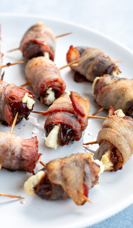 Bacon wrapped dates with goat cheese scattered all over a white plate and focused in on one date in the center.