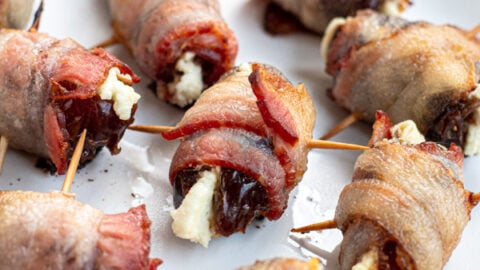 Bacon wrapped dates with goat cheese scattered all over a white plate and focused in on one date in the center.