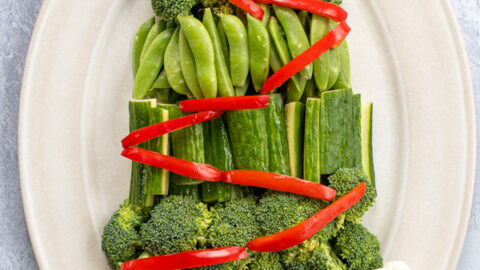 A platter containing a Christmas Tree Veggie Tray, green veggies are shaped to look like a tree with red bell pepper slices as decorations.