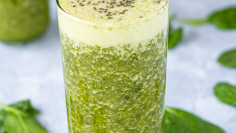 A large glass with a metal straw filled to the top with an energizing green smoothie, topped with chia seeds.
