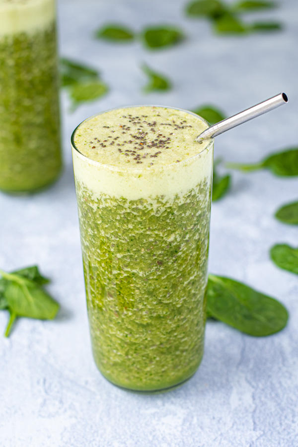 A large glass with a metal straw filled to the top with an energizing green smoothie, topped with chia seeds.