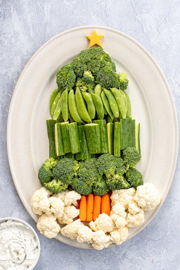 A tray with green vegetables shipped into a Christmas tree shape with carrot sticks as a base and cauliflower for snow.