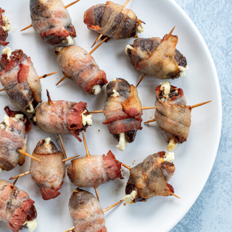 Overhead view of bacon wrapped dates with goat cheese on a white plate being held together by toothpicks.