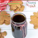 Pinterest Pin with text overlay 'Gingerbread Simple Syrup'. Image of a glass jar of dark colored syrup tied up with a red and white bow.