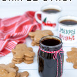 Pinterest Pin with text overlay 'Gingerbread Simple Syrup'. Image of a glass jar of dark colored syrup tied up with a red and white bow.