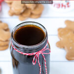 Pinterest Pin with text overlay 'Gingerbread Simple Syrup'. Image of a glass jar of dark colored syrup tied up with a red and white bow.