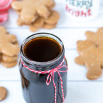 Pinterest Pin with text overlay 'Gingerbread Simple Syrup'. Image of a glass jar of dark colored syrup tied up with a red and white bow.