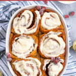 Pinterest Pin with text overlay 'Overnight Gingerbread Cinnamon Rolls'. Image of a baking dish filled with cinnamon rolls and topped with cream cheese frosting.
