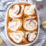 Pinterest Pin with text overlay 'Gingerbread Cinnamon Rolls'. Image of a baking dish filled with cinnamon rolls and topped with cream cheese frosting.