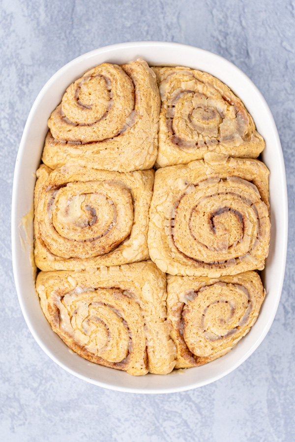 Risen cinnamon rolls in a white baking dish ready to be baked in the oven.