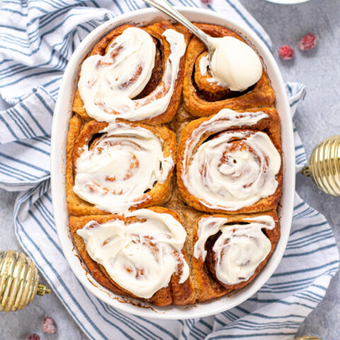 Fresh baked gingerbread cinnamon rolls with a spoon full of frosting.