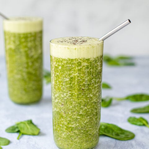 Two large glasses full of bright energizing green smoothie, topped with chia seeds and with a metal straw.