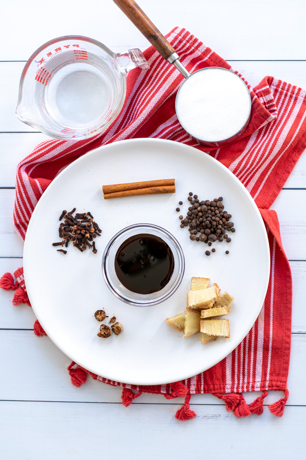 All the ingredients needed to make gingerbread simple syrup on a plate and measuring cups, including whole spices, sugar, and water.
