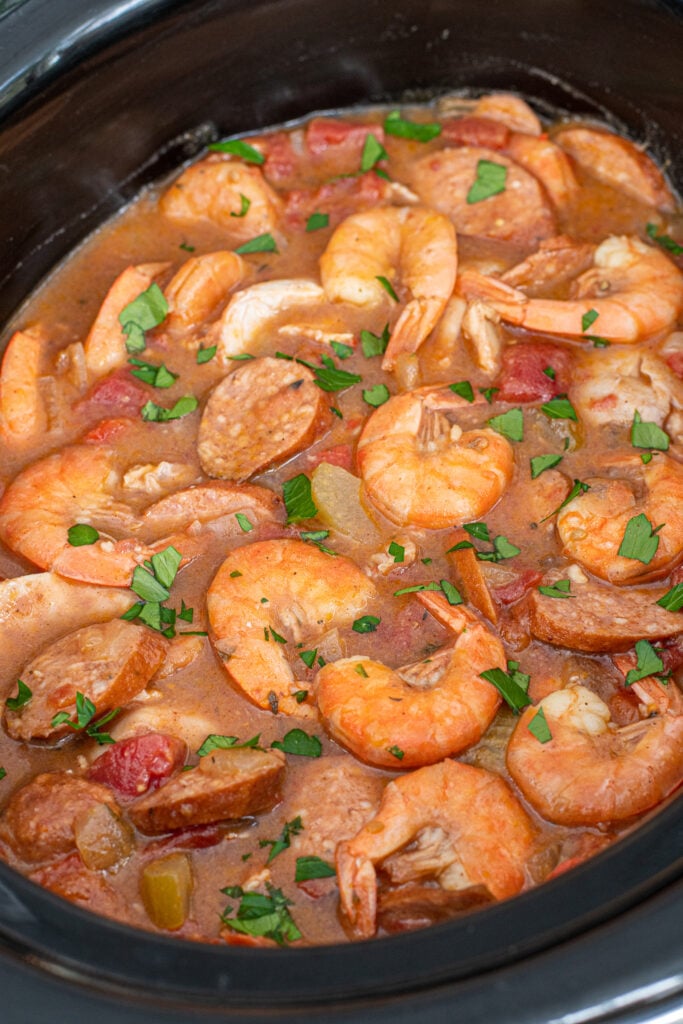 Close look inside a crockpot filled with cooked gumbo with shrimp and andouille sausages on the top.