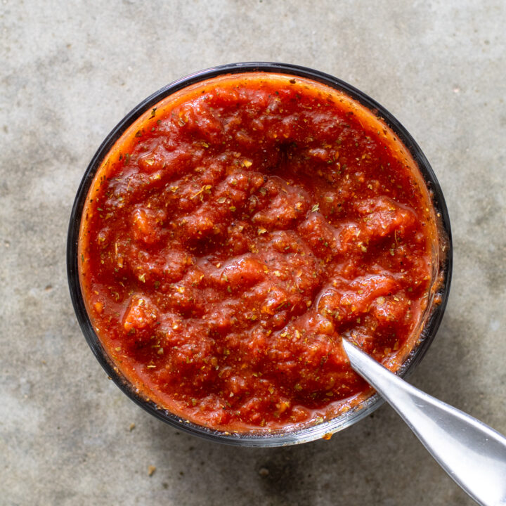 Small glass bowl with freshly mixed pizza sauce with a spoon.