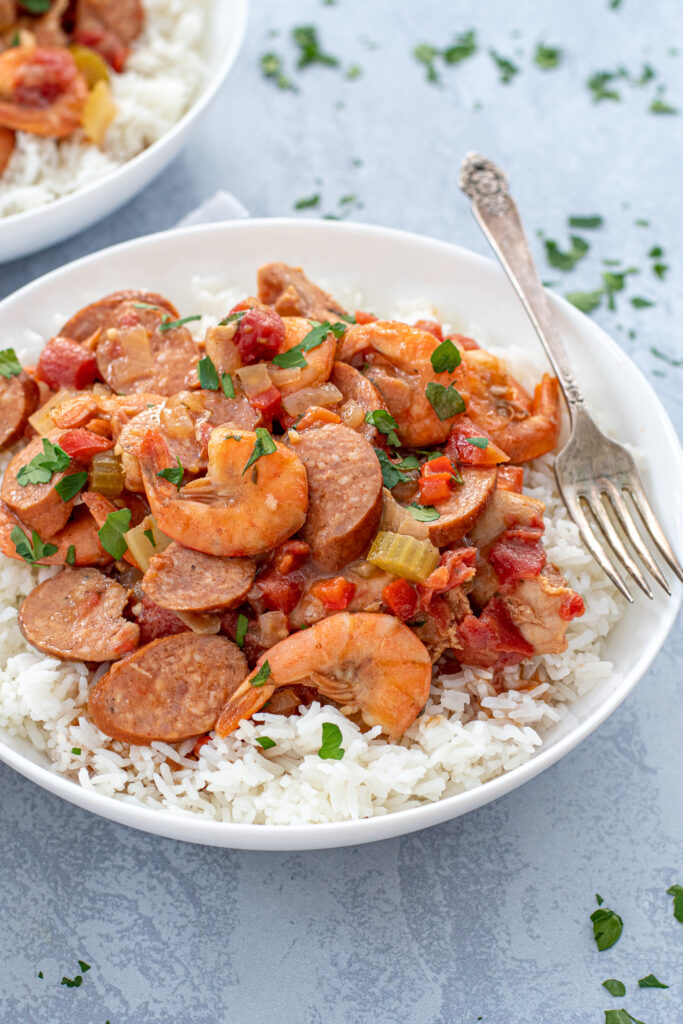 Close up of a bowl of red gumbo on top of a bed of rice with a fork.