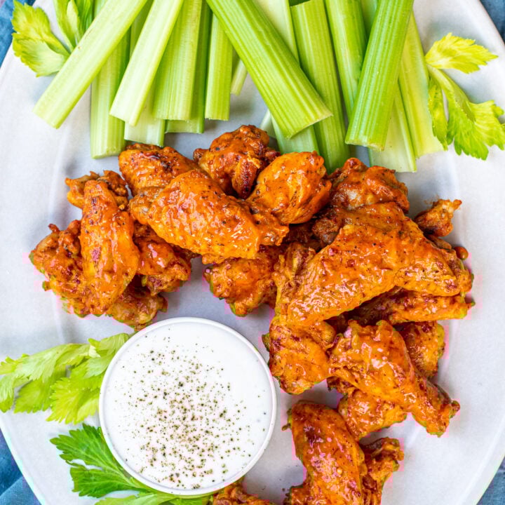 Chicken wings made in the instant pot and sauced and piled up on a white platter next to a bunch of celery and a cup of ranch sauce.