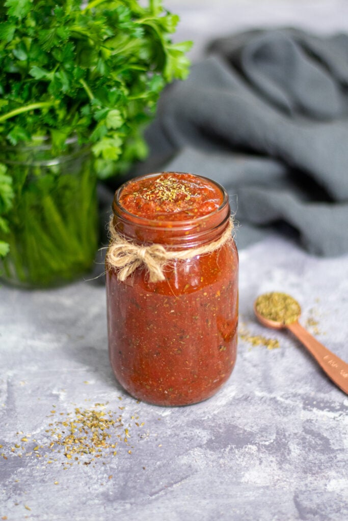 Glass jar tied with a little bow filled to the brim with homemade pizza sauce.