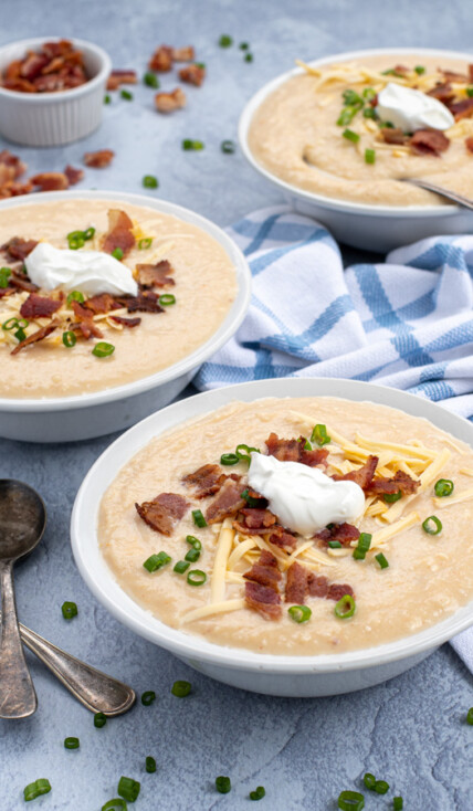 Instant Pot Loaded Baked Potato Soup in three bowls shown at an angle topped with cheese, bacon, green onions, and sour cream they are sitting next to a pile of spoons.