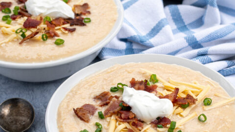 Instant Pot Loaded Baked Potato Soup in three bowls shown at an angle topped with cheese, bacon, green onions, and sour cream they are sitting next to a pile of spoons.