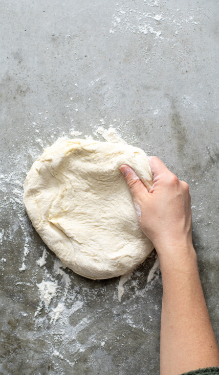 Hand grabbing at a ball of freshly risen homemade pizza dough.