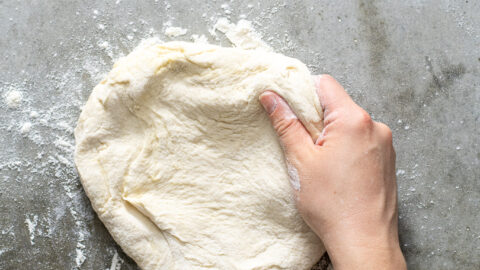 Hand grabbing at a ball of freshly risen homemade pizza dough.