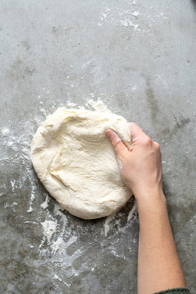 Hand grabbing at a ball of freshly risen homemade pizza dough.