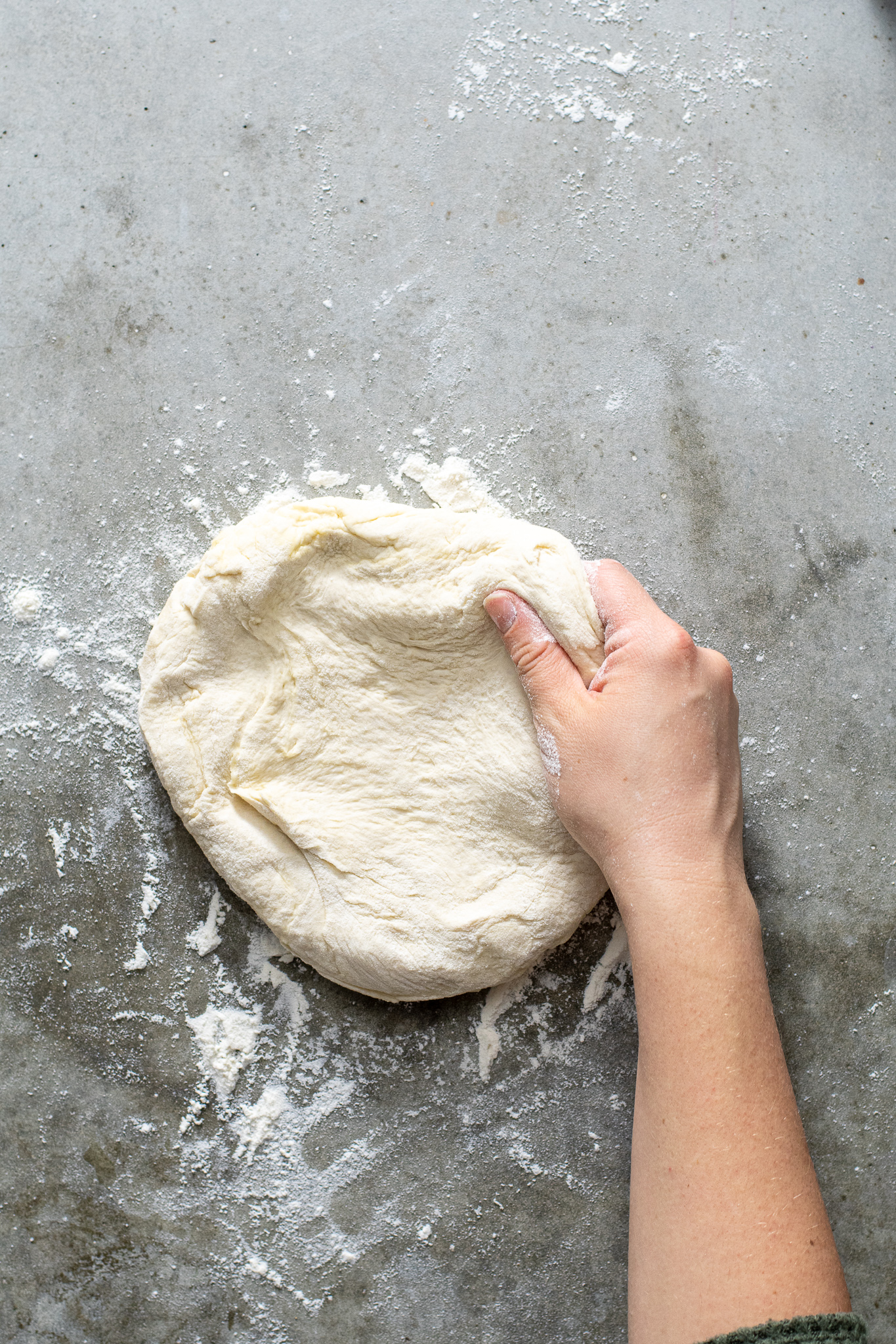 Hand grabbing at a ball of freshly risen homemade pizza dough.