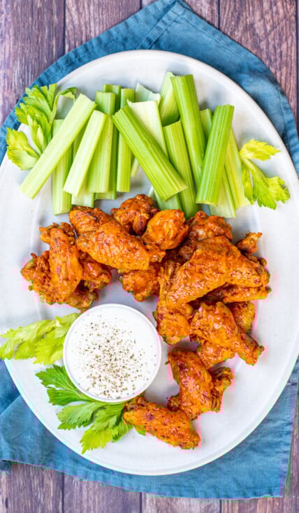 A large white platter holding pressure cooker hot wings, celery and a cup of ranch dressing.