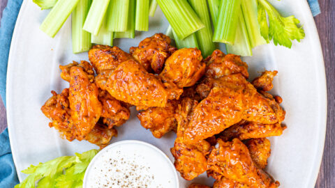 A large white platter holding pressure cooker hot wings, celery and a cup of ranch dressing.