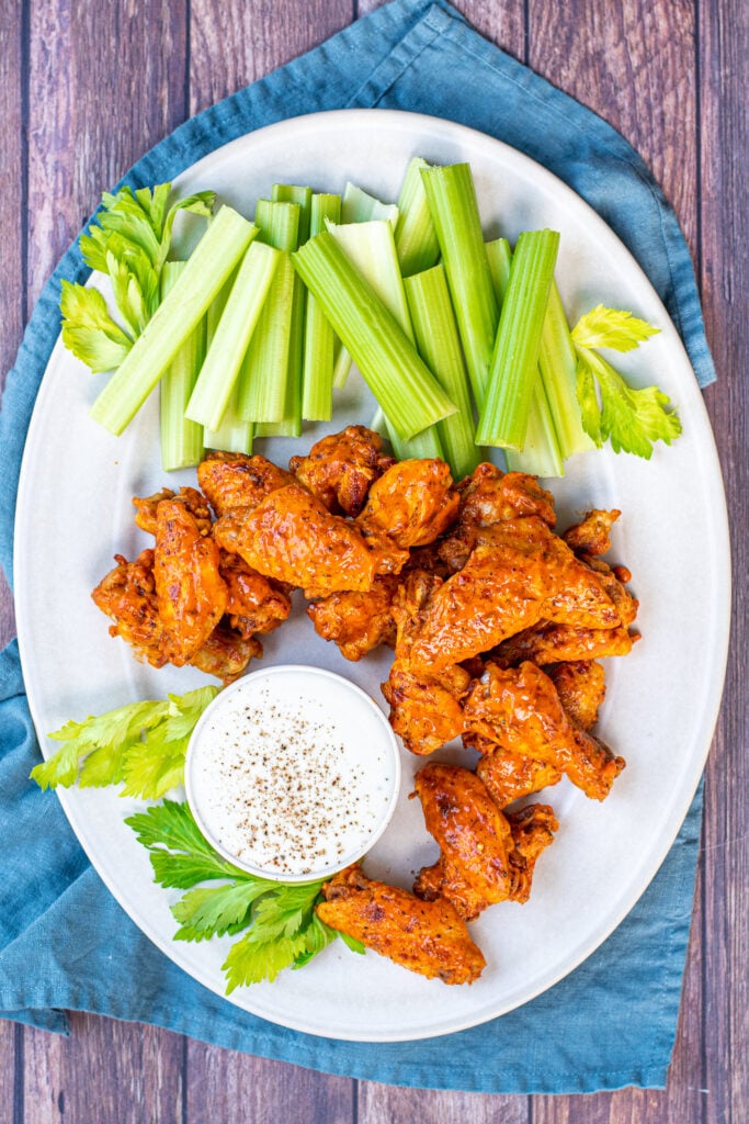 A large white platter holding pressure cooker hot wings, celery and a cup of ranch dressing. 