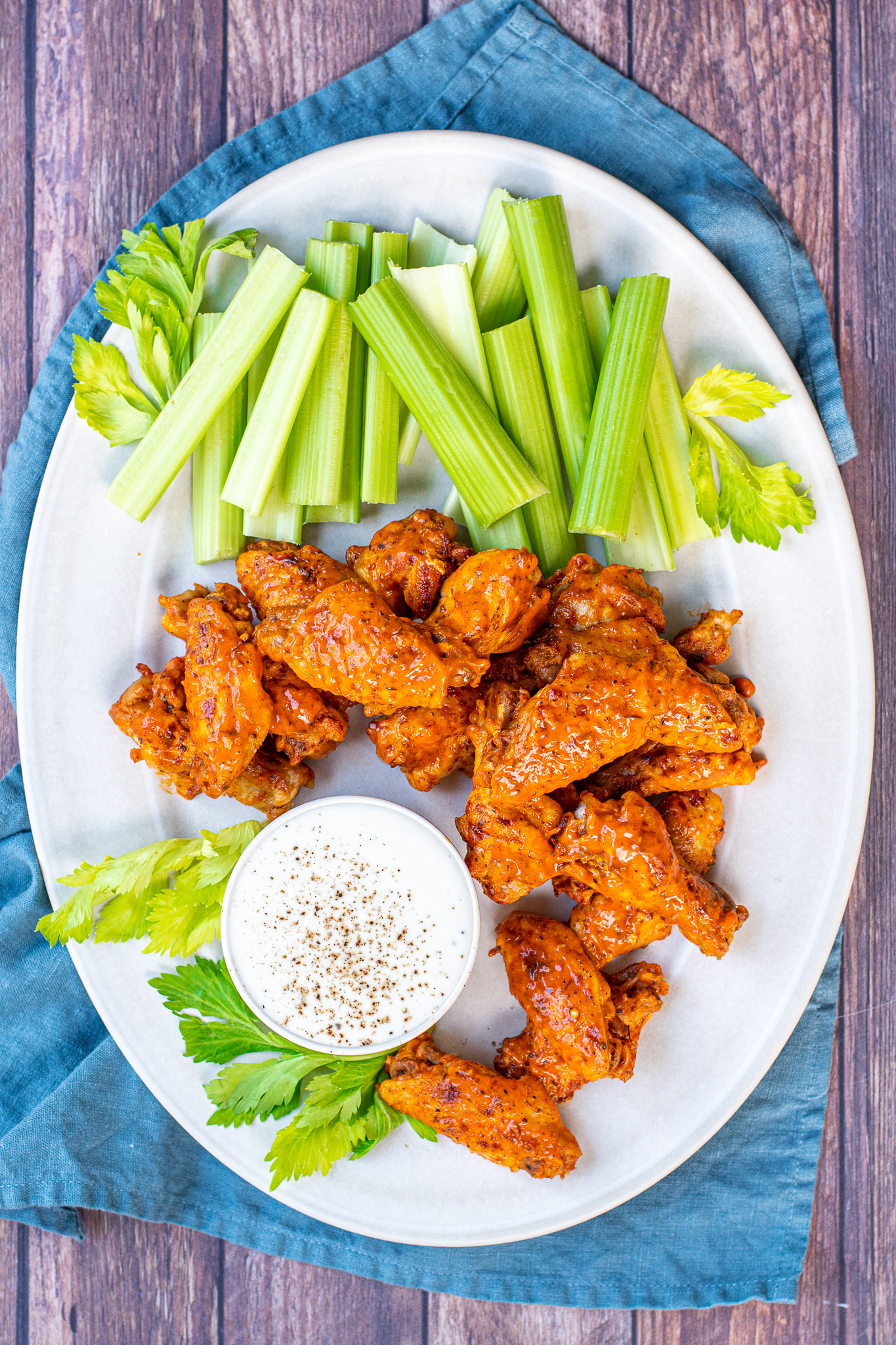 A large white platter holding pressure cooker hot wings, celery and a cup of ranch dressing.