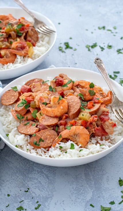 A large white bowl with a large scoop of gumbo on top of a bed of white rice with a fork.