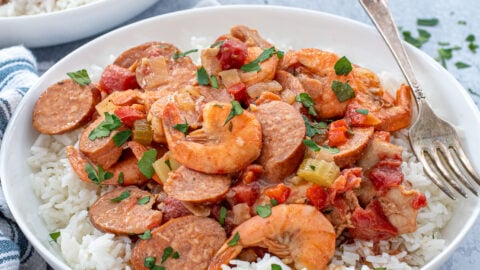 A large white bowl with a large scoop of gumbo on top of a bed of white rice with a fork.