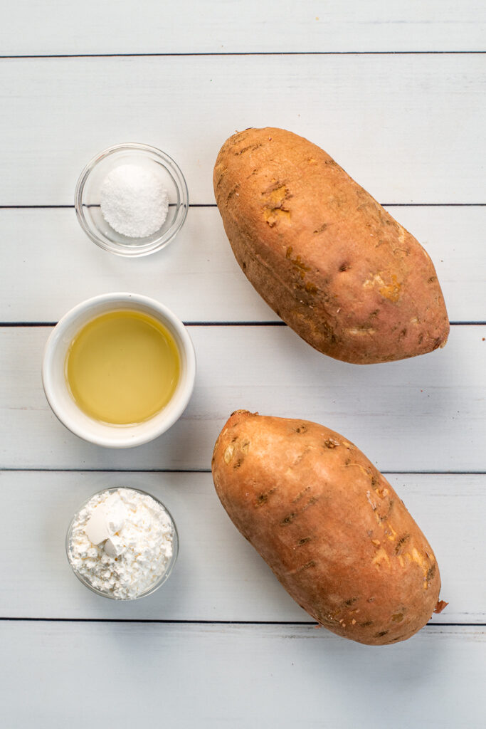 The 4 ingredients needed to make sweet potato wedges on a white background, sweet potatoes, oil, salt, and cornstarch.