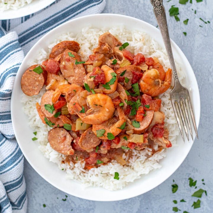 Overhead of a large white bowl full of white rice and red gumbo piled high on top showing off shrimp, sausages, and chicken.