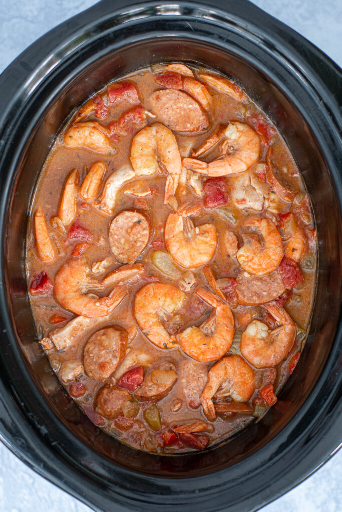 Overhead view of a crockpot filled with cook gumbo including cooked shrimp on the top.