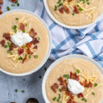 Pinterest Pin for with text overlay 'Loaded Baked Potato Soup in the Pressure Cooker'. Image of bowls of garnished baked potato soup and spoons.