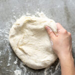 Pinterest Pin with text overlay 'Homemade Pizza Dough'. Image of the dough being stretched by hand.