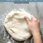 Pinterest Pin with text overlay 'Homemade Pizza Dough'. Image of a hand grabbing at a ball of pizza dough starting to stretch it into a crust.