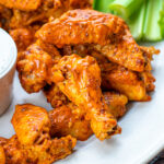Pinterest Pin with text overlay 'Hot Wings in the Instant Pot'. Image of platter with pile of saucy chicken wings next to dipping sauce.