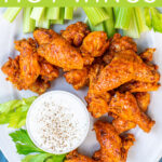 Pinterest Pin with text overlay 'Instant Pot Hot Wings'. Image of platter with pile of saucy chicken wings next to dipping sauce.
