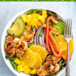 Pinterest Pin with text overlay 'Shrimp Salad with Avocado, Mango, & an Orange Vinaigrette'. Image of large bowl filled with mixed greens, grilled shrimp, avocado, and oranges.